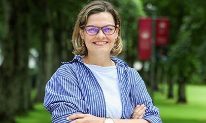 woman smiling at camera in front of trees on college campus