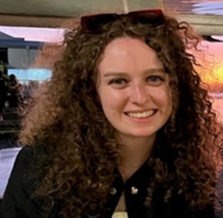 a young woman with brown curly hair smiling and wearing sunglasses on her head