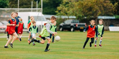 Two groups of children in green and red bibs play Gaelic Football