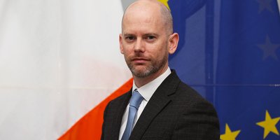 Cillian O'Kelly's headshot in front of the Irish and EU flags.
