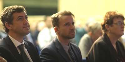 three people sitting in audience of conference listening to a speaker
