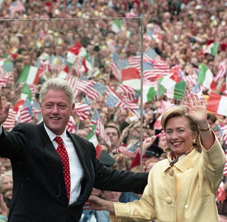 man and woman in a light yellow suit waving with a large crowd behind them waving irish and american flags