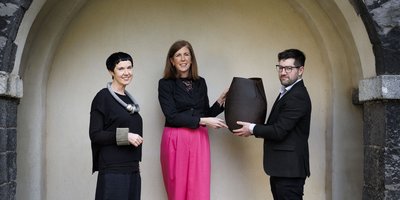 Two women and a man holding a sculpture in a stone archway