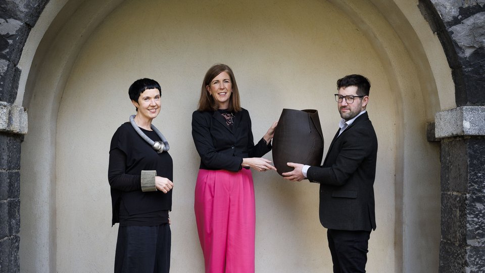 Two women and a man holding a sculpture in a stone archway