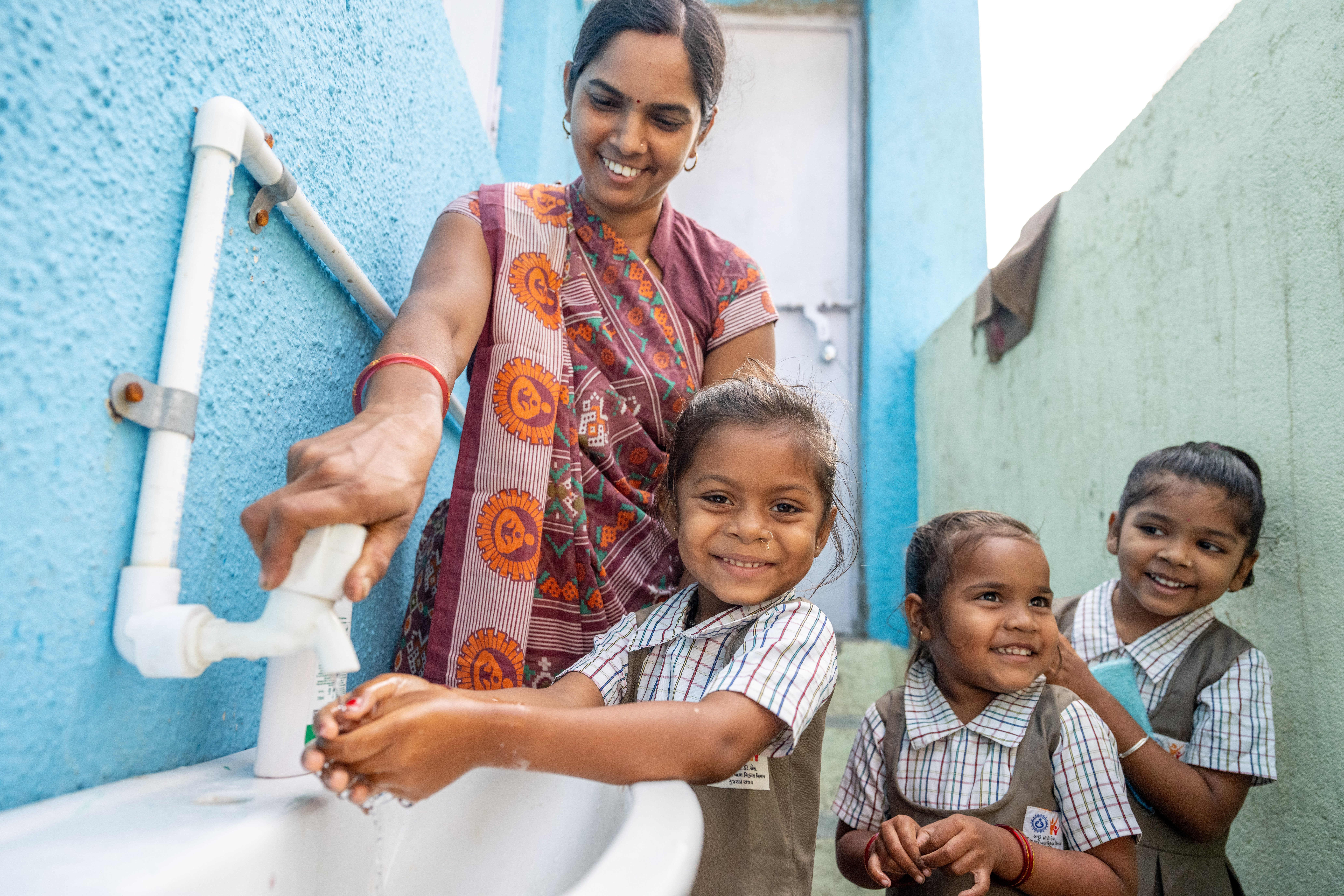 A community health worker in India helping a child turn on a water tap
