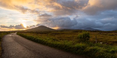 The Connemara Bog Road, with the sun setting behind a mountain visible in the distance.