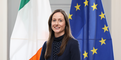 Janice McGann headshot in front of Ireland and EU flags.