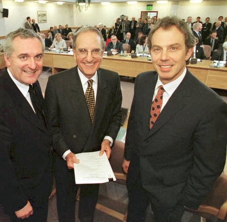 three men in suits smiling at the camera with crowds behind them