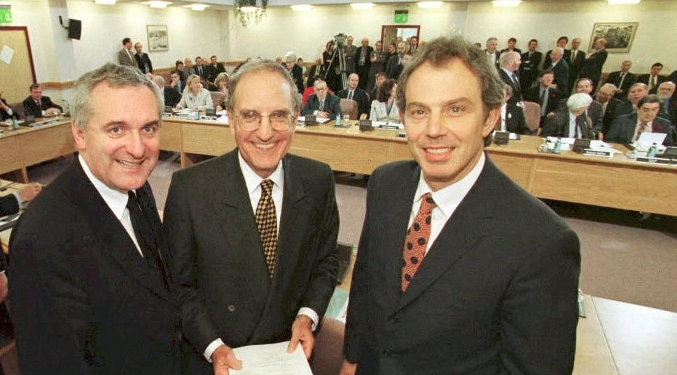 three male politicians facing and smiling at the camera with people behind them in the distance