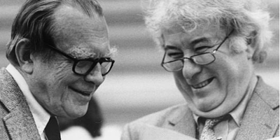 two men smiling looking at a book in a black and white photograph