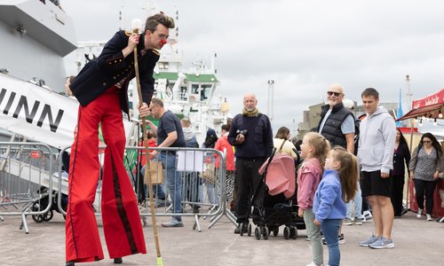 Man on stilts in a costume talking to children about boats