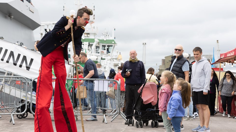 Man on stilts in a costume talking to children about boats