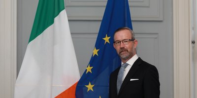 アイルランドとEUの国旗の前に立つスーツ姿の男性。