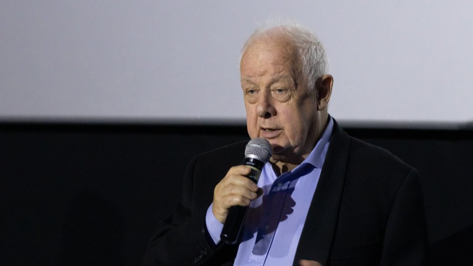 Irish filmmaker Jim Sheridan holding a microphone on a stage