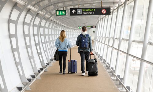 Two people walking in an airport with suitcases, pictured from behind