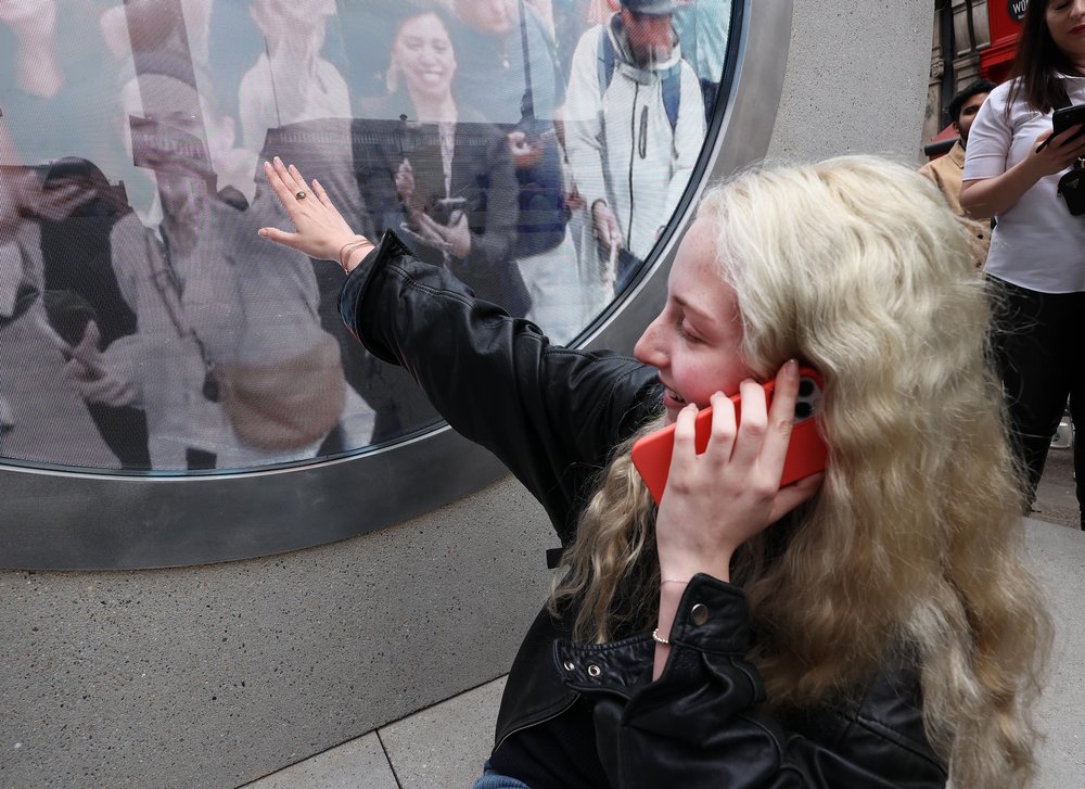 A woman on the phone reaching out to touch the Portal, while someone on the other side reaches back towards her.