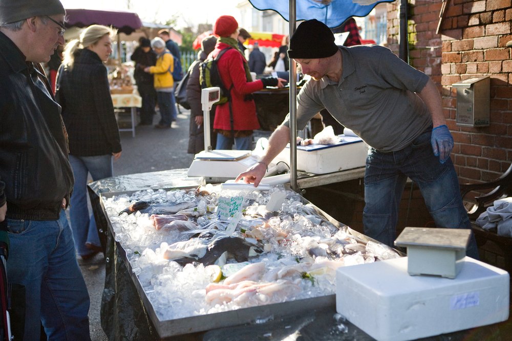a fishmonger speaking to customers at an outdoor market