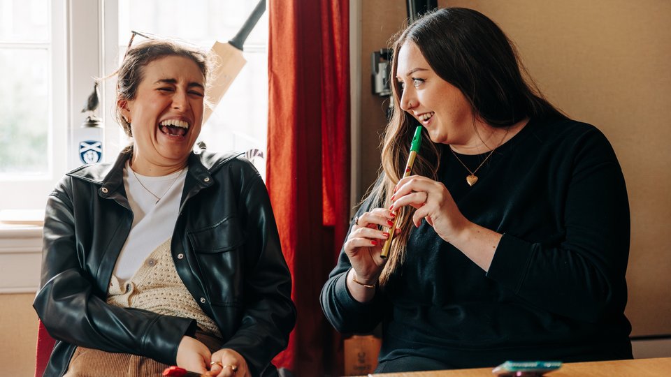 Two women laughing together as one plays the tin whistle.