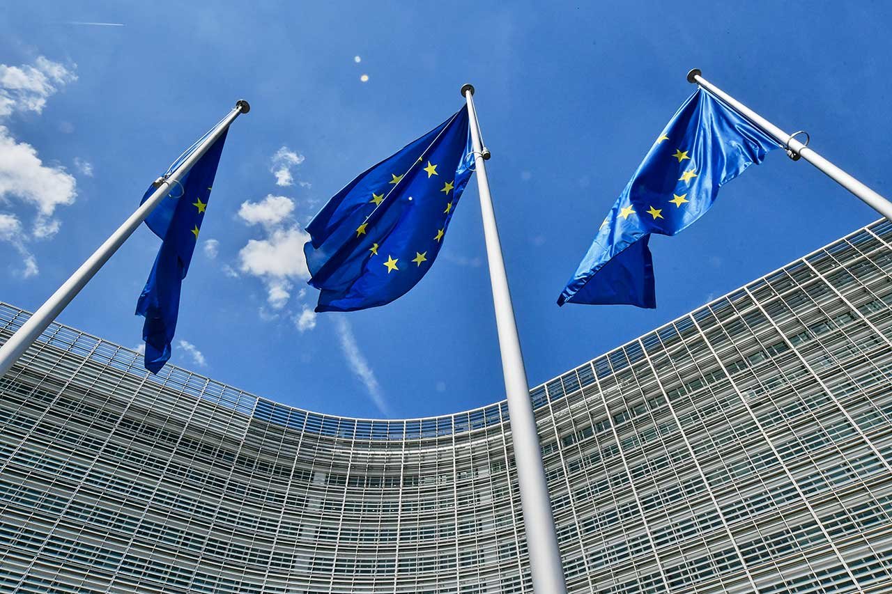Three blue flags with yellow stars in front of a large office building
