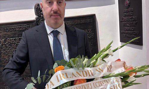 Deputy HOM, Brendan Farrell holding flowers, in front of a nameplate commemorating Eileen Frances Short-Garlinska