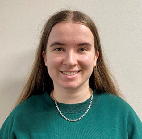 a young woman looking directly at the camera wearing a teal jumper and a necklace