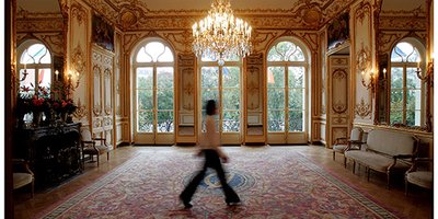 A blur of a woman walking through a reception room in the Embassy.
