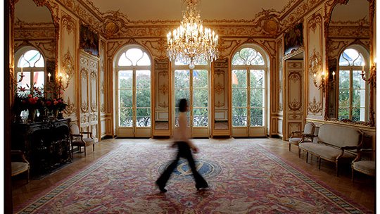 A blur of a woman walking through a reception room in the Embassy.