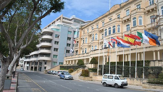 View of the exterior of the Embassy building with flags flying outside.