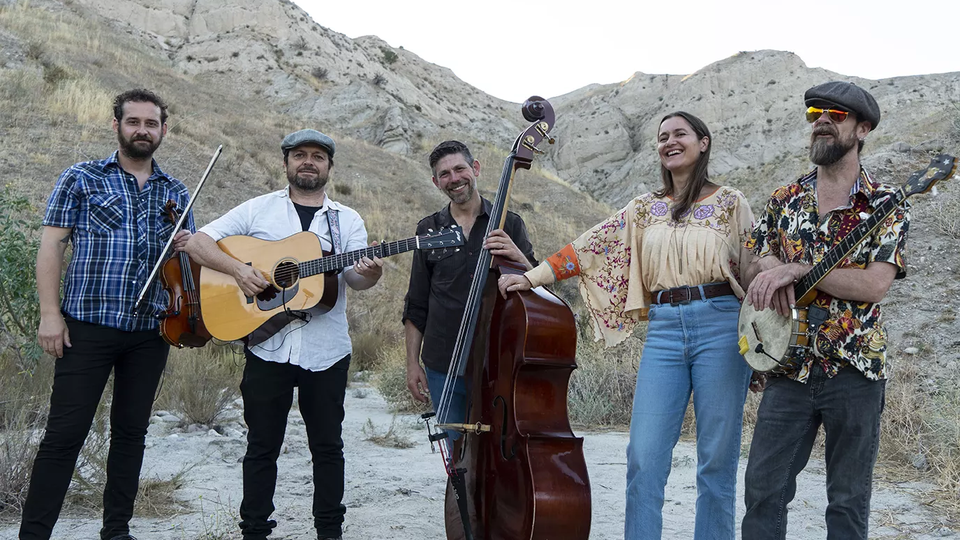 five musicians in a canyon, four men and one women, carrying a variety of string instruments