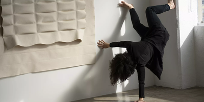 one woman dressed in black upside down leaning on one arm with legs against a white wall