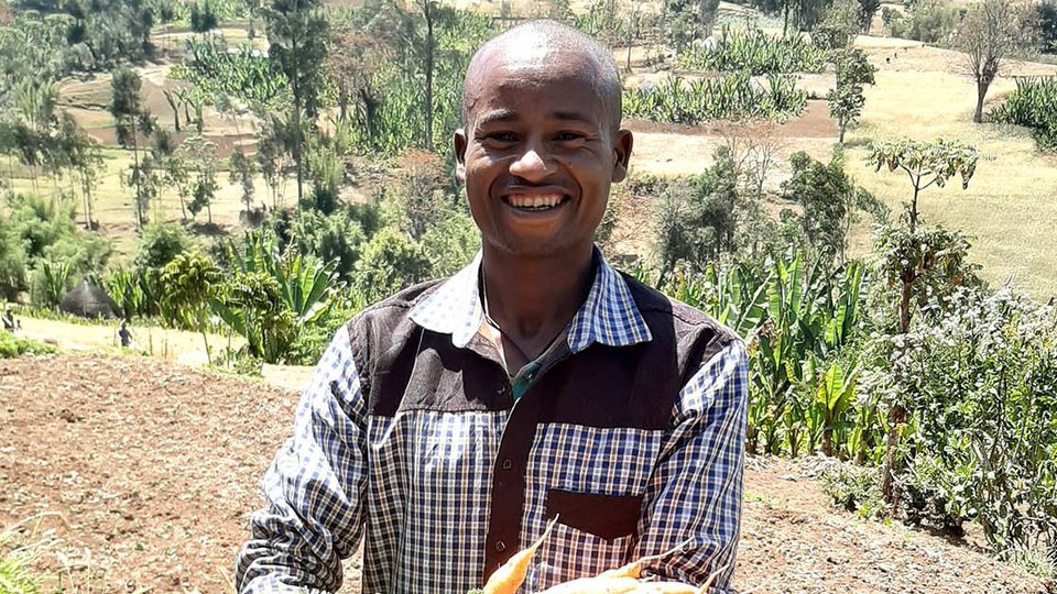 A man holds a large bunch of root vegetable as he stands in a tilled field.