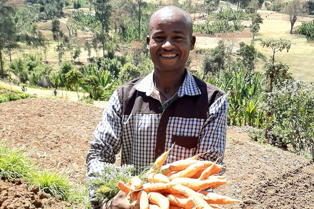 A man holds a large bunch of root vegetable as he stands in a tilled field.