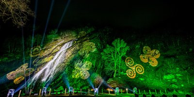 Powerscourt Waterfall lit up in green at night, with celtic designs cast onto it.