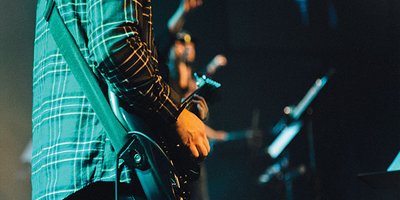 Zacherie Fiesen dressed in a plaid shirt, playing guitar on stage, viewed from the side.