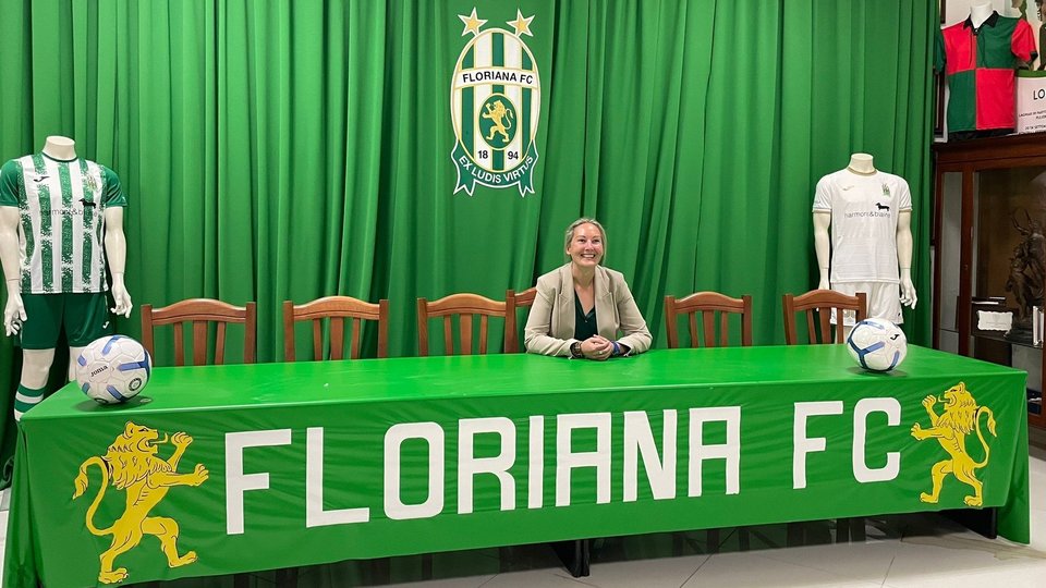 A woman sitting behid a press conference table reading Floriana FC
