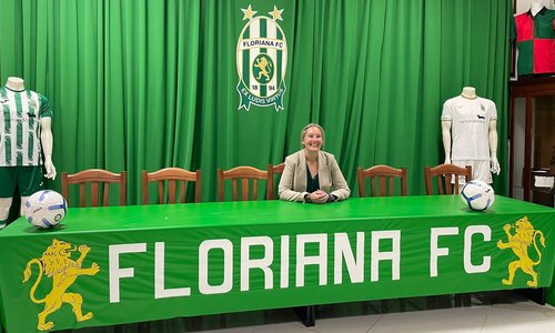 A woman sitting behid a press conference table reading Floriana FC