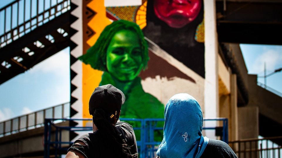 Two artists viewed from behind, looking up at the mural of female Senegalese sportstars they have just painted