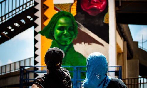 Two artists viewed from behind, looking up at the mural of female Senegalese sportstars they have just painted