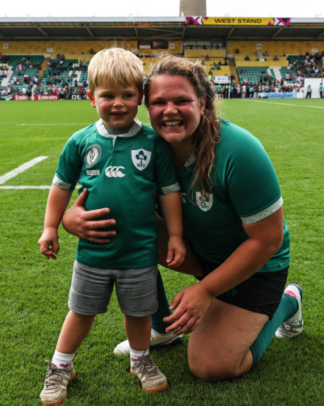 Rugby player posing with her young son on the pitch