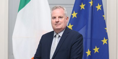 Headshot of Consul General Cathy Geaghan standing in front of the Irish and EU flags.