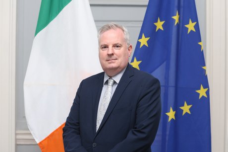 Headshot of Gerry Kelly in front of the EU and Irish flags