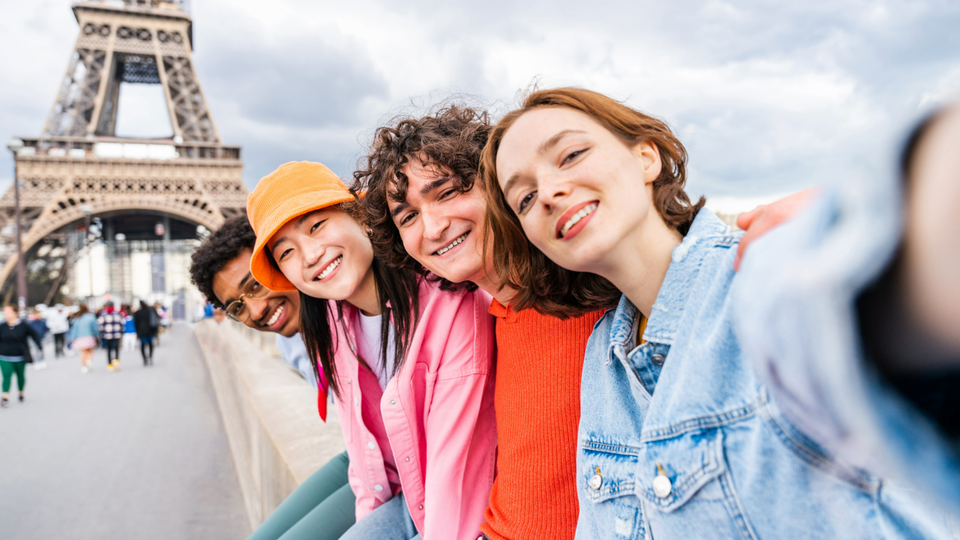 Group of four young people taking a selfie in front of the Eiffel Tower