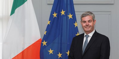 Ambassador Martin Fraser standing in front of the Irish and EU flags.