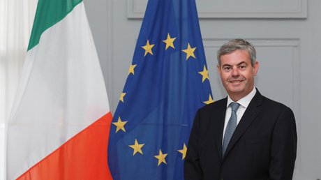 Ambassador Martin Fraser standing in front of the Irish and EU flags.