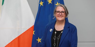 Headshot of Michelle Winthrop standing in front of the Irish and EU flags.