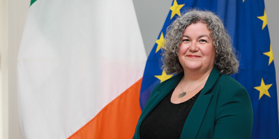 Headshot of Consul General Cathy Geaghan standing in front of the Irish and EU flags.