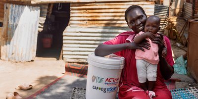 Mary Isaac Chol sits with her baby beside a container from the handwashing kit, which helps her provide safe water for her family with support from Irish Aid and Trócaire.