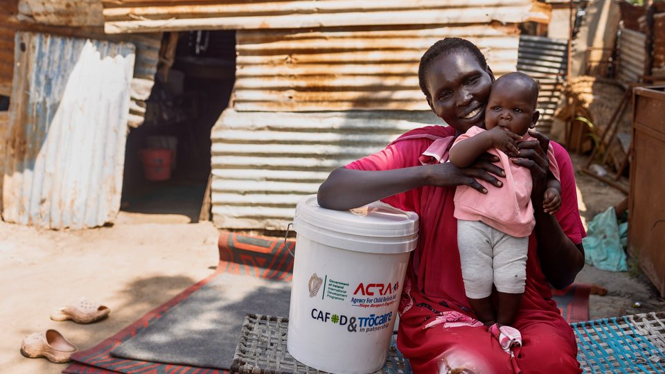 Mary Isaac Chol sits with her baby beside a container from the handwashing kit, which helps her provide safe water for her family with support from Irish Aid and Trócaire.