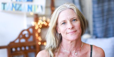 Helen Espey standing in front of fabrics with a sign reading 'Handmade in Tanzania' behind her
