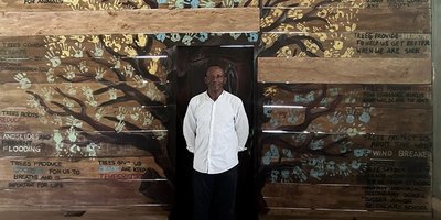 Tommy Garnett stood in front of a mural of a tree where the leaves are all children's handrpints